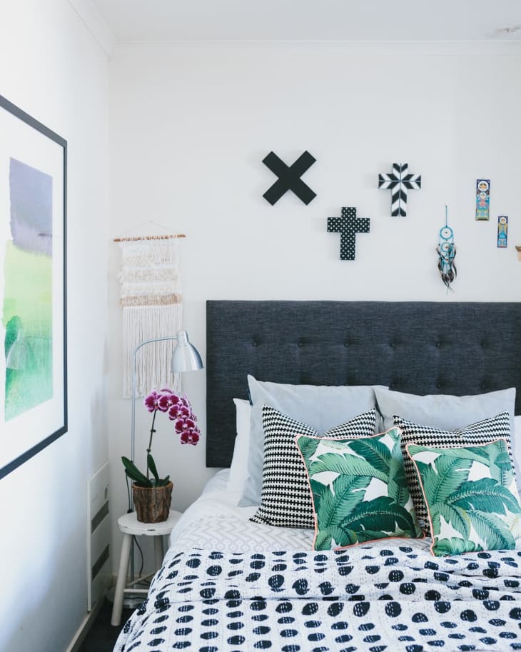 Bedroom with a gray headboard, tropical leaf pillows, orchid plant, and geometric wall decor.