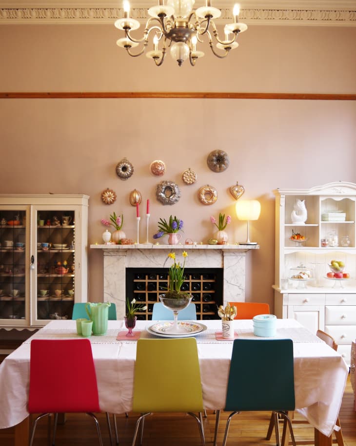 Dining room with colorful chairs, white tablecloth, marble fireplace, decorative plates, and a chandelier.