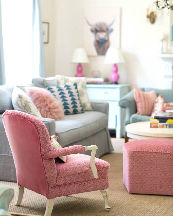 Living room with pink armchair, matching ottoman, gray sofa, patterned pillows, and a bull painting on the wall.