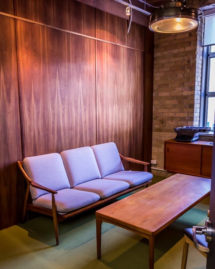 Mid-century modern room with a wooden sofa, light cushions, matching coffee table, and industrial pendant light.