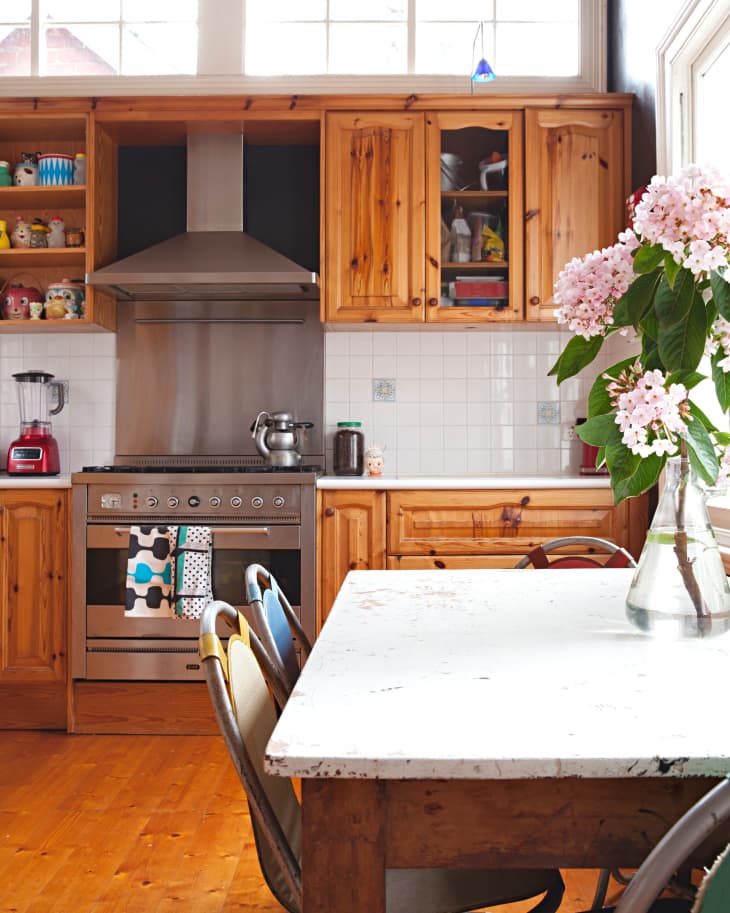 Rustic kitchen with wooden cabinets, stainless steel stove, white table, and pink flowers in a vase.