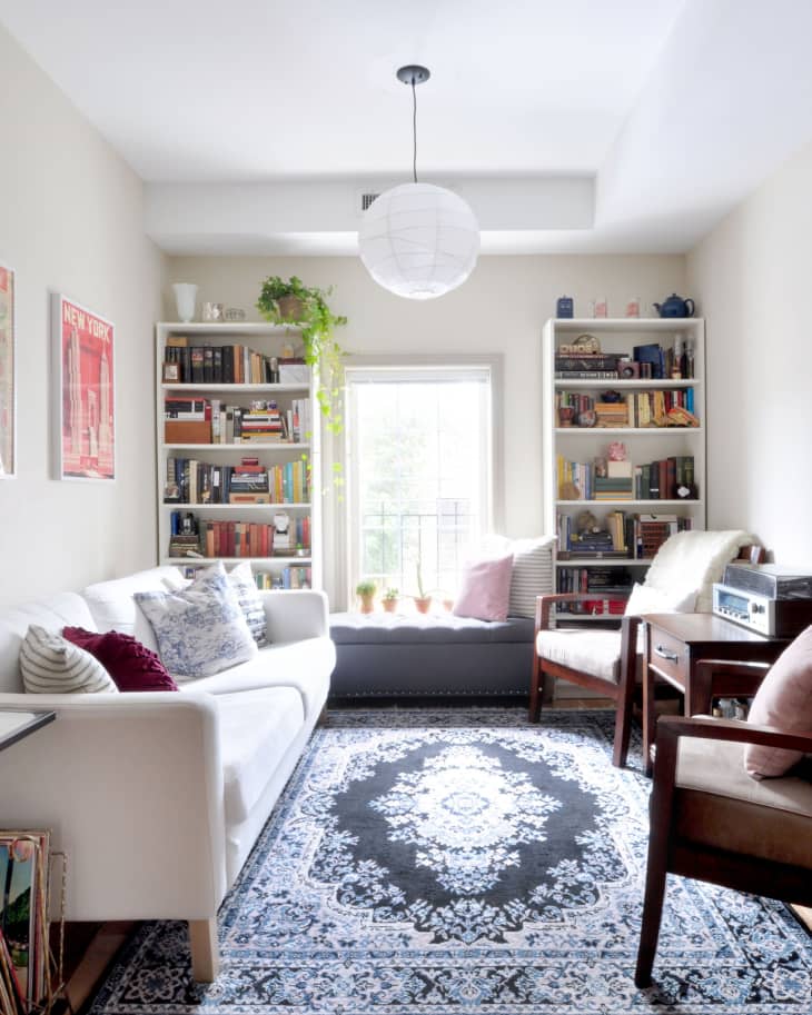 Living room with white sofa, patterned rug, bookshelves, and a window seat with cushions.