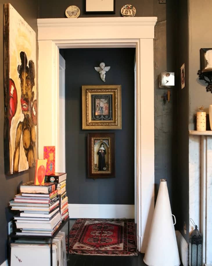 Hallway with dark walls, framed art, a red patterned rug, and a stack of books on the left.