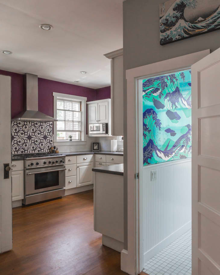 Kitchen with purple accent wall, white cabinets, stainless steel stove, and a vibrant blue and green mural in the hallway.