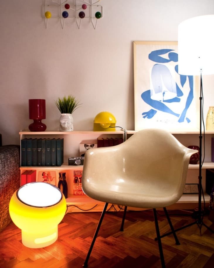 Mid-century modern room with a beige chair, yellow lamp, colorful wall art, and a blue abstract painting.