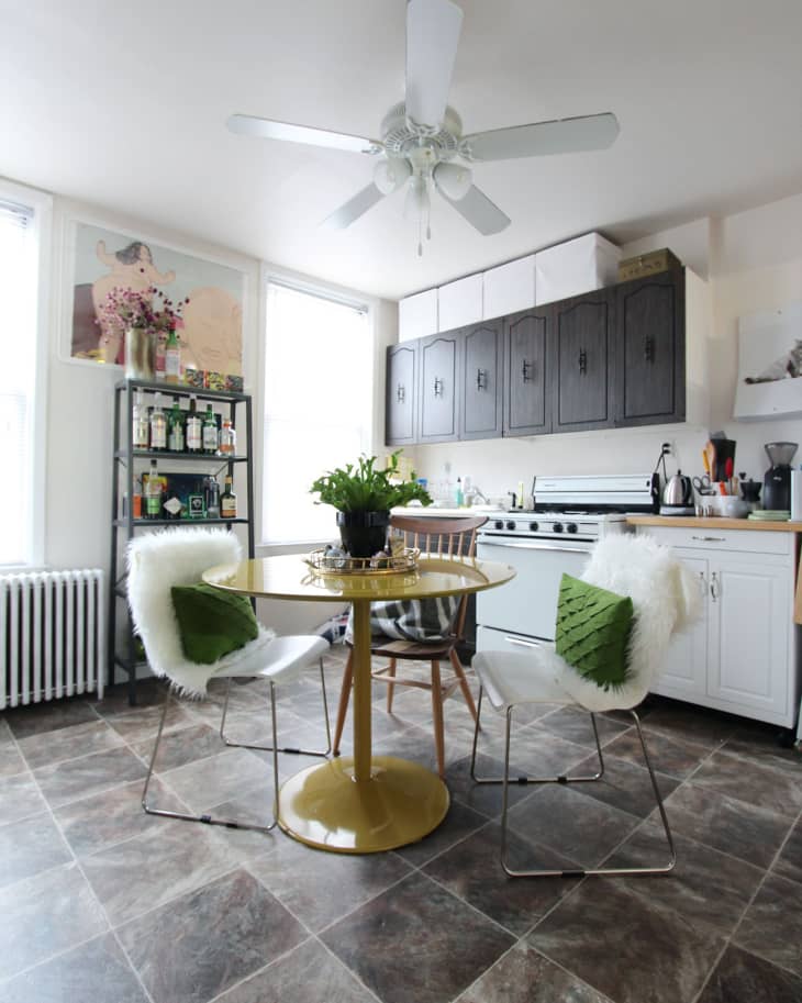 Kitchen with yellow round table, white chairs with green pillows, black cabinets, and a ceiling fan.