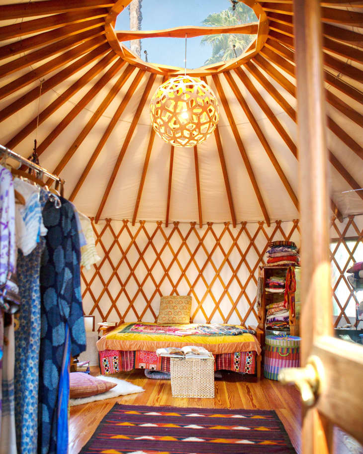 Cozy yurt interior with a colorful bed, woven basket, patterned rug, and a geometric light fixture under a skylight.