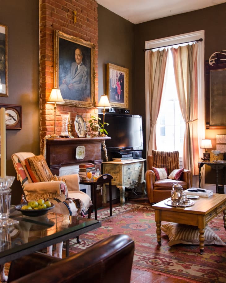 Cozy living room with brick fireplace, vintage decor, armchairs, and a patterned rug.