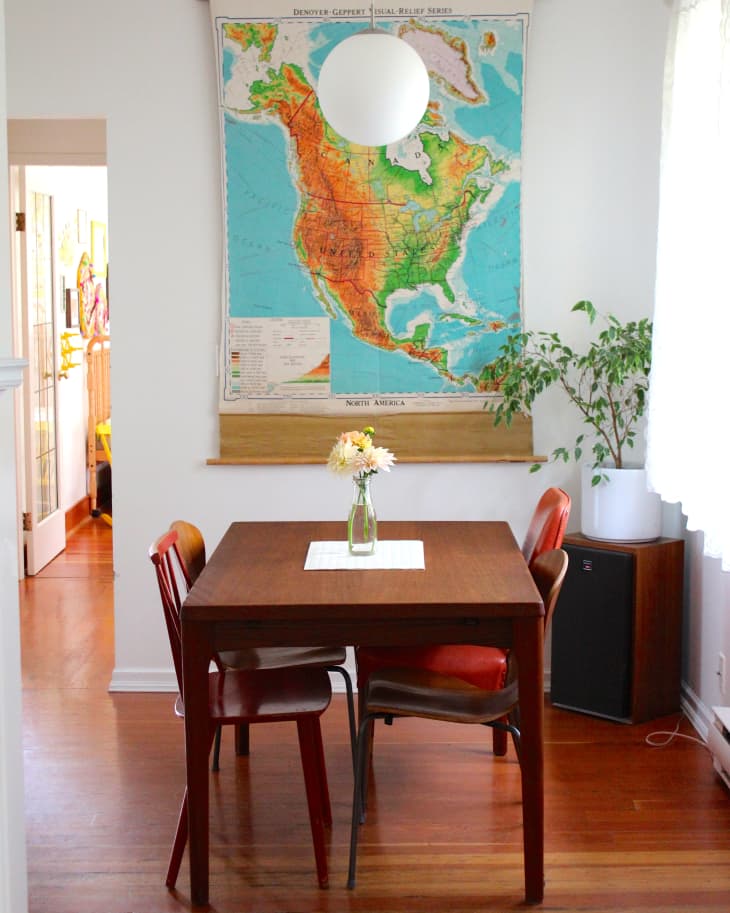 Dining area with a wooden table, red chairs, a vase with flowers, and a large map of North America on the wall.