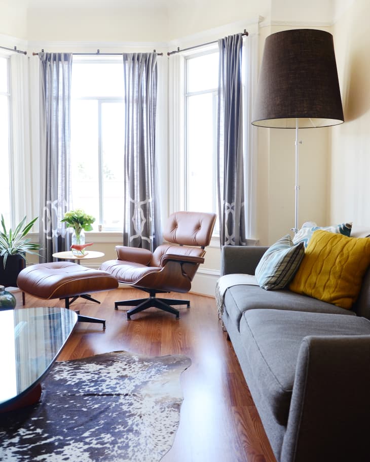 Living room with a brown leather lounge chair, gray sofa, yellow pillow, large floor lamp, and cowhide rug.