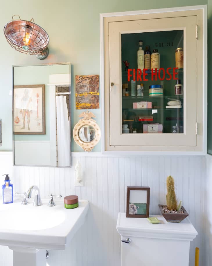 Bathroom with a pedestal sink, wall mirror, vintage light, and a cabinet labeled "Fire Hose" containing toiletries.
