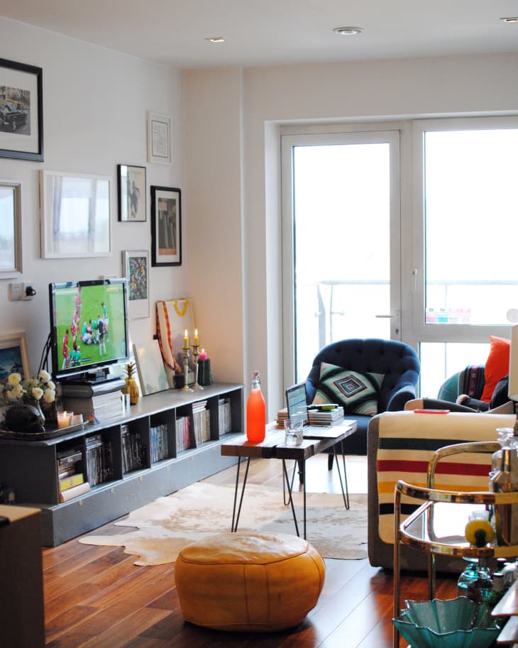 Cozy living room with a TV, art on walls, a blue armchair, striped sofa, and a small table with a red bottle.