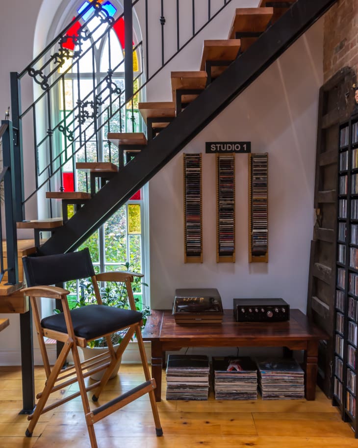 Staircase with stained glass window, director's chair, vinyl records, and CDs in a cozy studio corner.