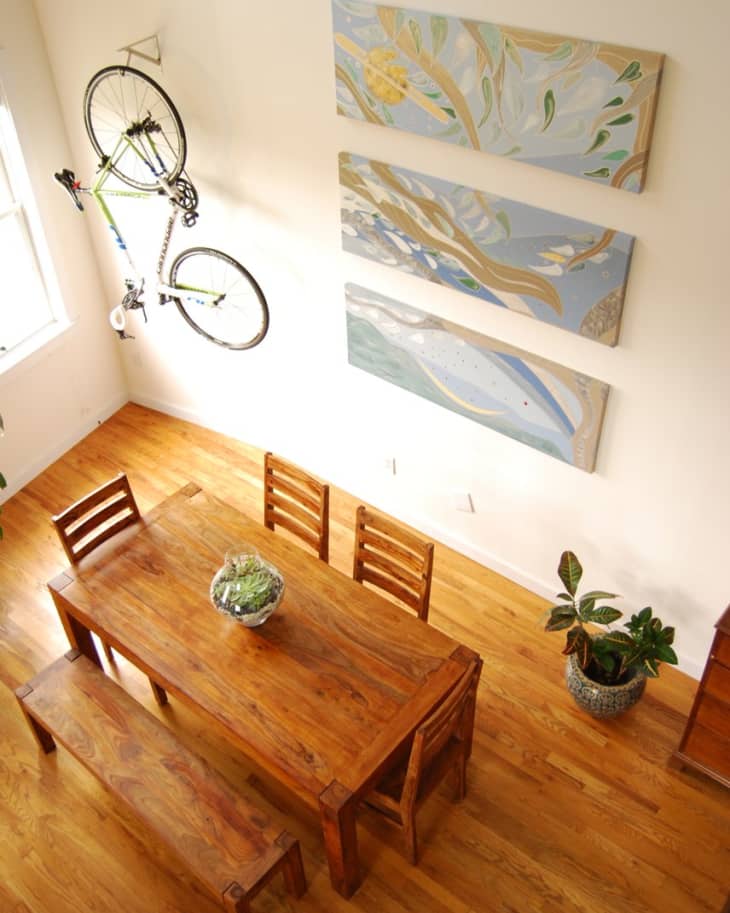 Dining room with wooden table, chairs, bench, wall art, and a bicycle mounted on the wall.