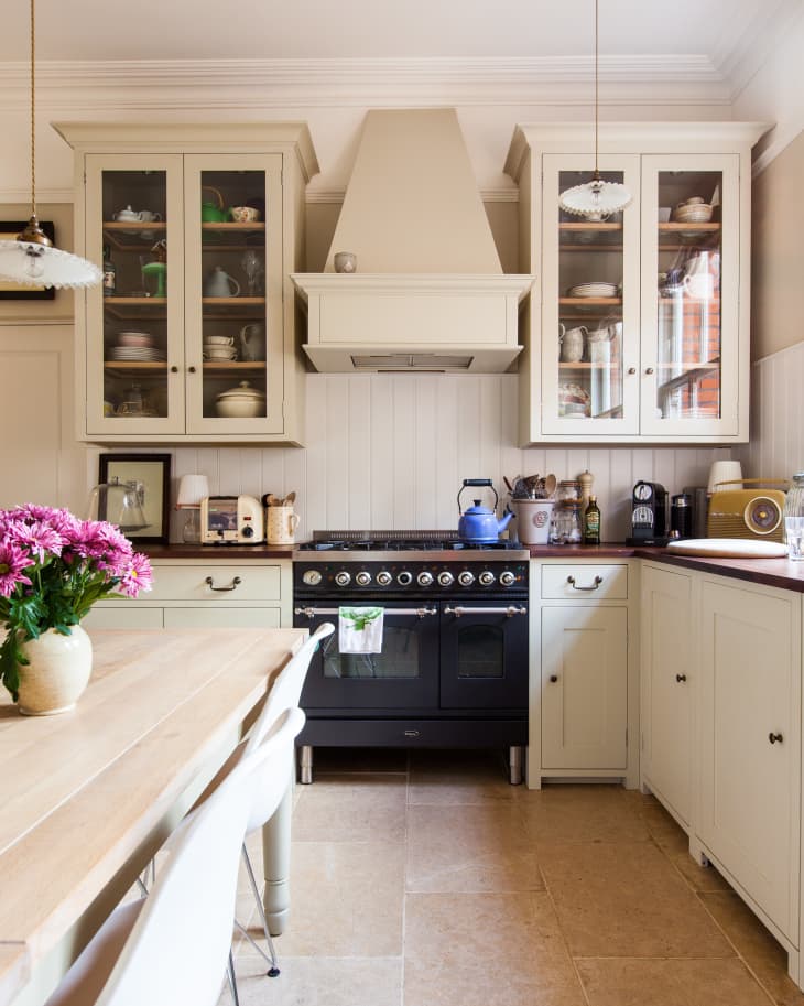 Traditional kitchen with cream cabinets, black stove, wooden table, white chairs, and pink flowers in a vase.