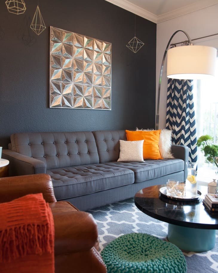 Gray tufted sofa with orange and white pillows, geometric wall art, and a round coffee table in a modern living room.