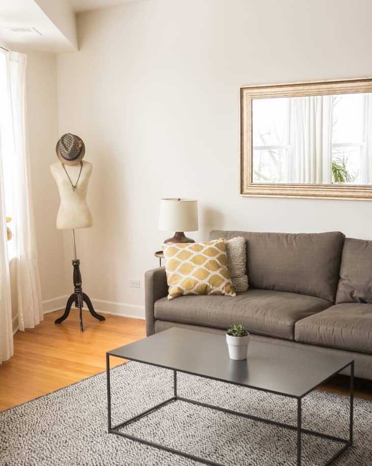 Living room with gray sofa, yellow patterned pillow, mannequin, black coffee table, and wall mirror.