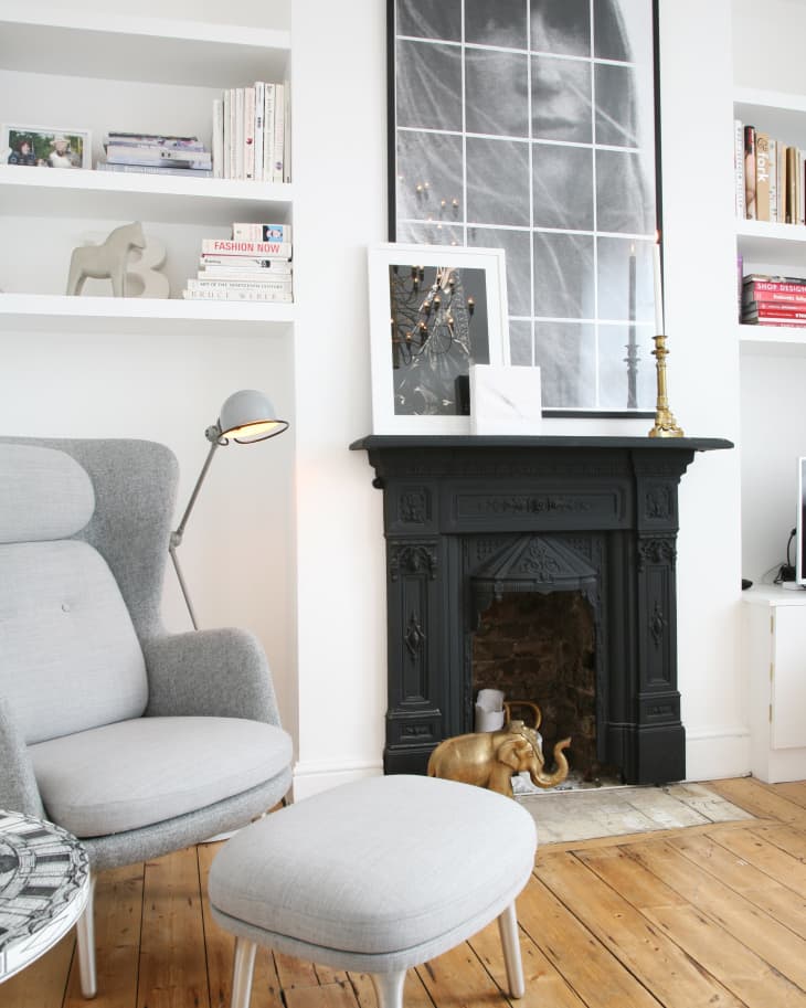 Cozy living room with a gray armchair, ottoman, black fireplace, and decorative elephant statue on wooden floor.