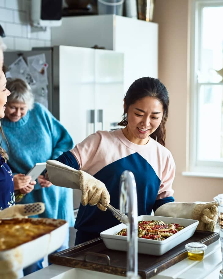 Woman serving home made food in busy family kitchen and smiling