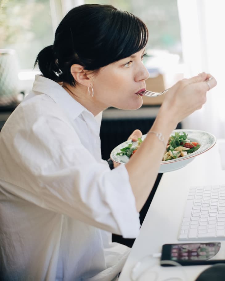 Businesswoman eating pasta while looking at computer in home office.