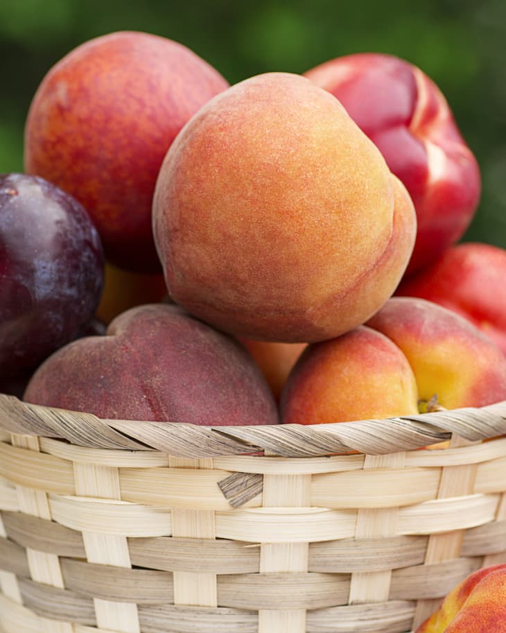 Wicker basket filled with a bounty of stonefruit including peaches, nectarines, and plums.