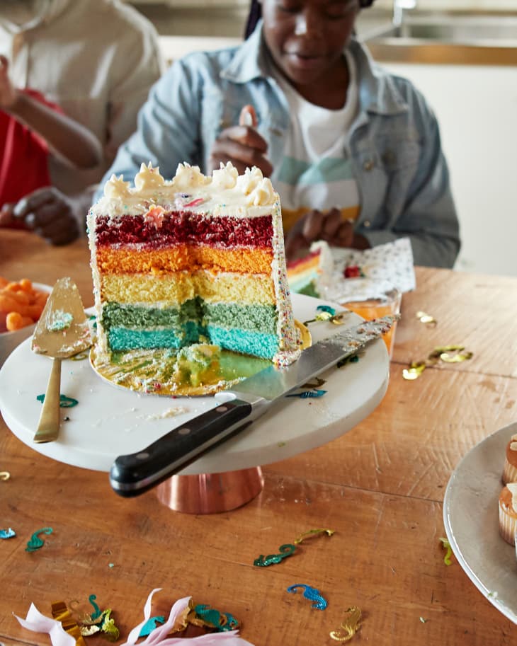 Multi colored cake on table while teenage girl sitting in background during birthday party