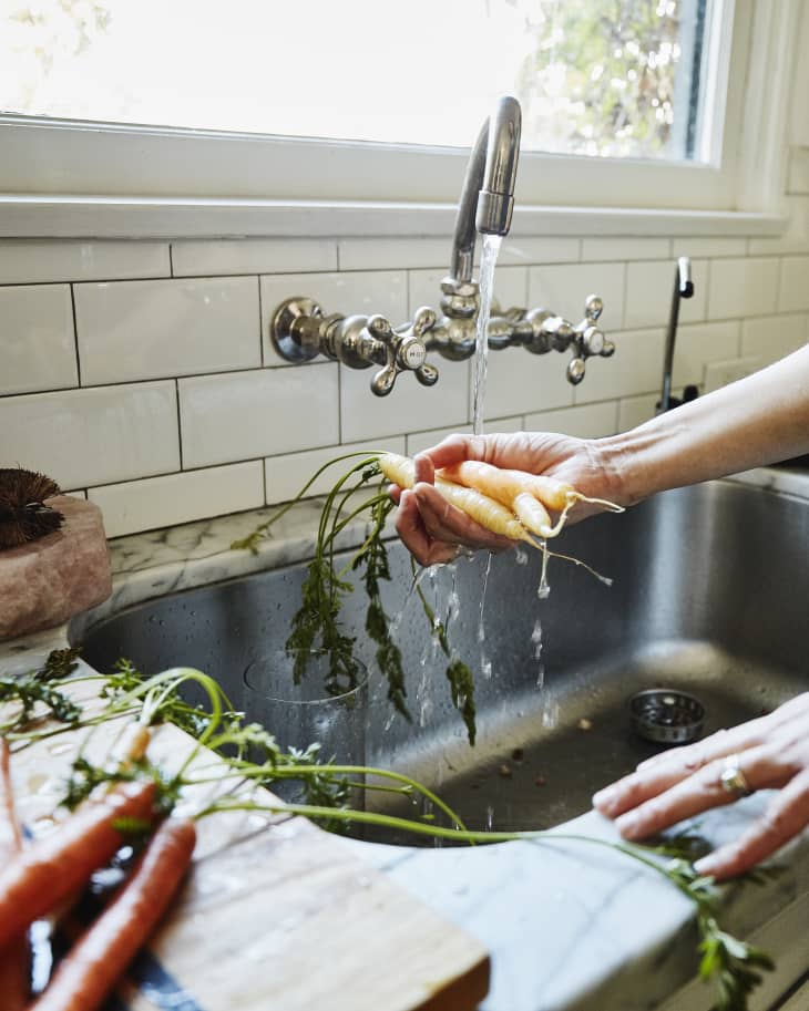 Woman washing organic carrots at kitchen sink