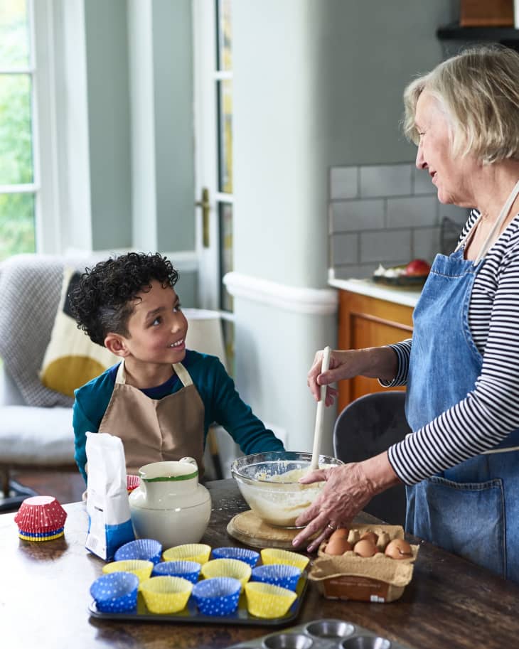 Grandmother making cupcakes with young boy at table in kitchen, learning, togetherness, domestic life.
