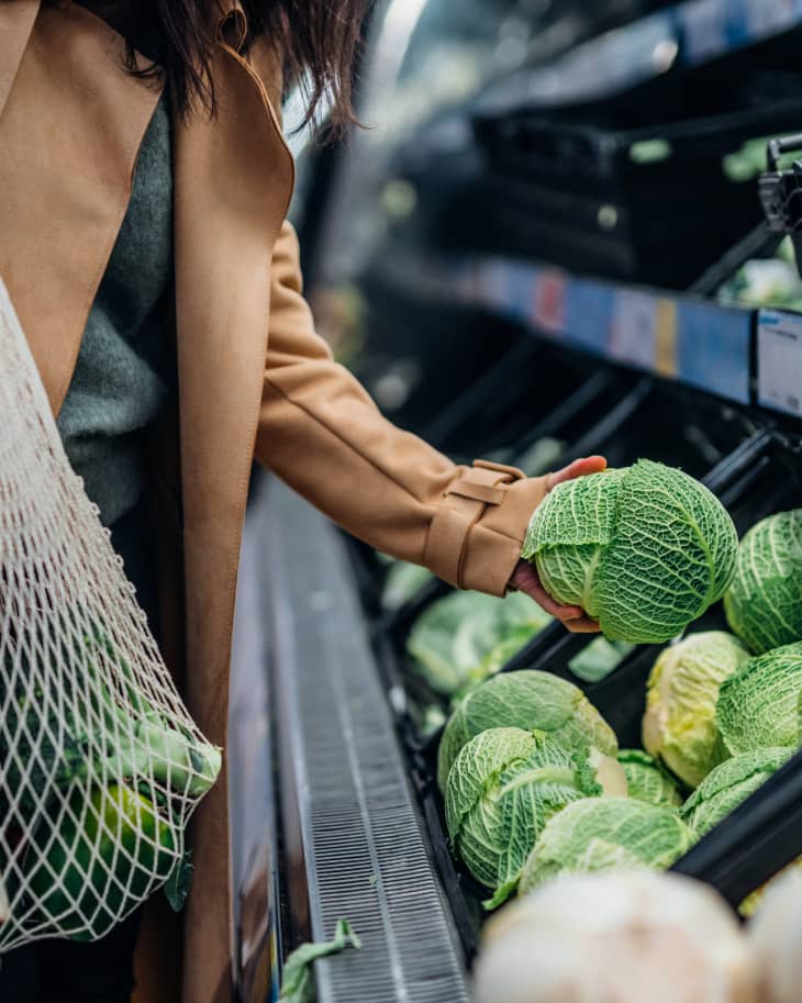 Cropped shot of woman shopping for fresh fruits and organic vegetables in supermarket. Putting a cabbage into an eco-friendly cotton mesh shopping bag. Zero waste concept.