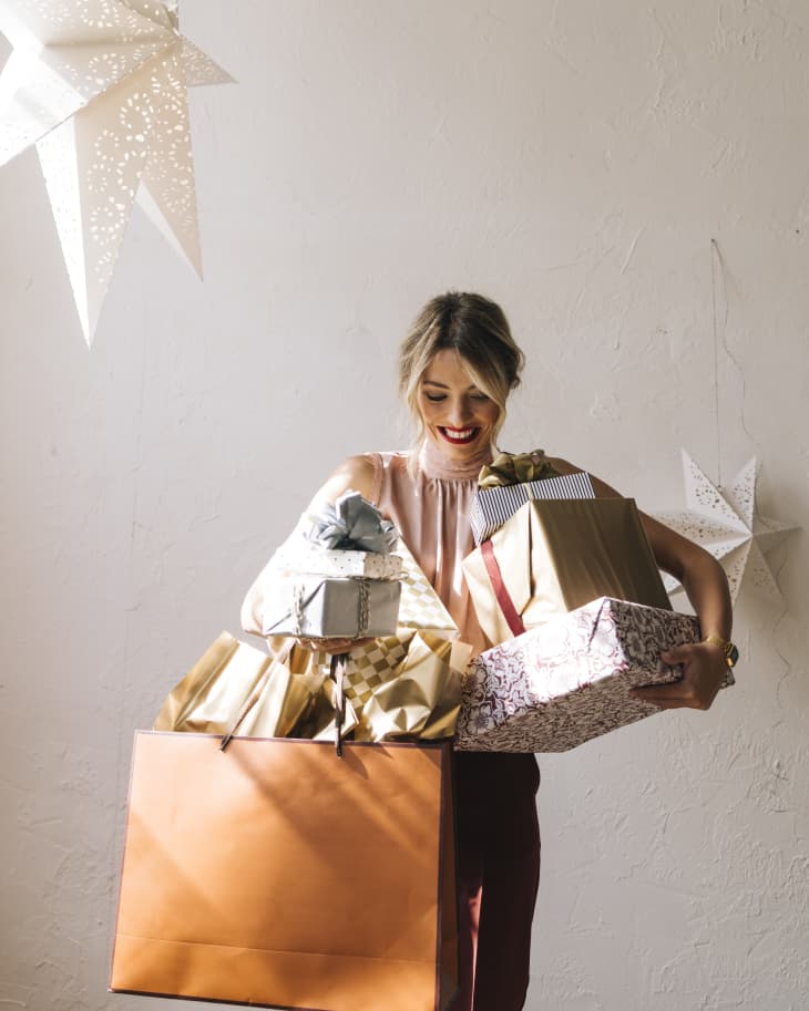 woman holding many gifts in bags and boxes and smiling. Paper stars above her as decorations