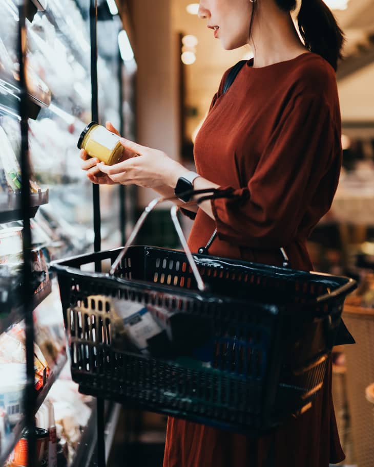 Woman carrying a shopping basket, standing along the dairy aisle, reading the nutrition label on the bottle of a fresh organic healthy yoghurt.