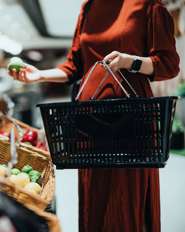 Woman carrying a shopping basket, grocery shopping for fresh organic fruits and vegetables in supermarket.