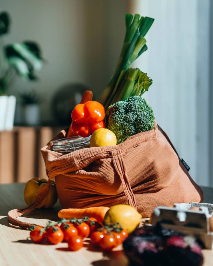 Eco-friendly reusable shopping bag with multi-coloured fresh vegetables and groceries on the table at home. Shopping with reusable grocery bag for plastic free and waste-free life. Responsible shopping. Zero waste and sustainable lifestyle concept
