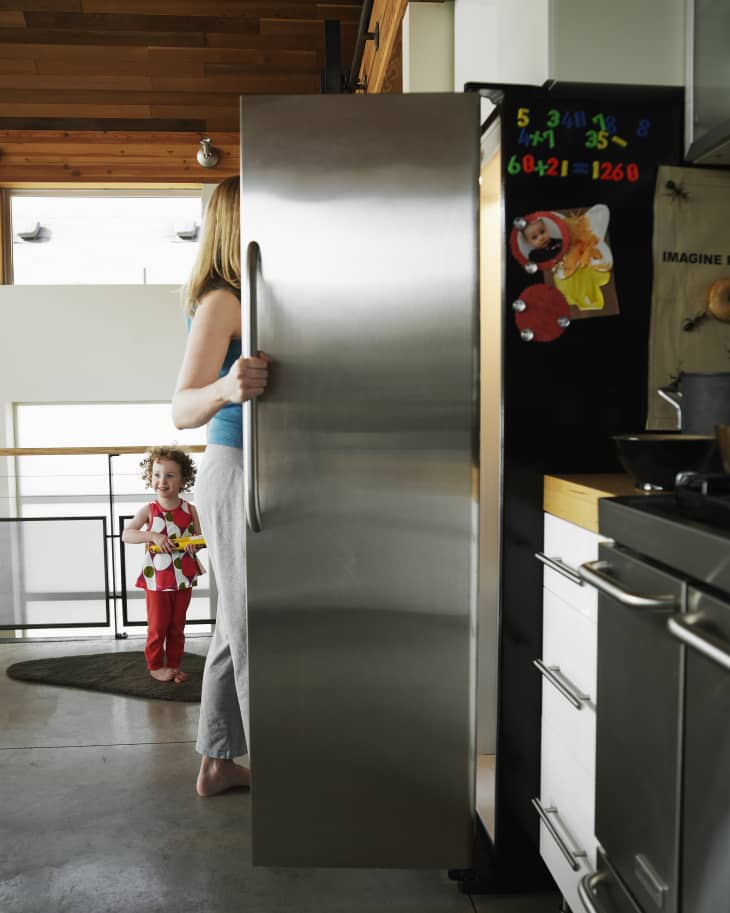 Mother reaching in refrigerator in home kitchen daughter smiling in background