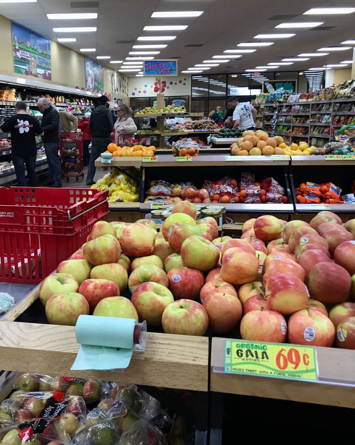 The interior of the produce section of a Trader Joe’s grocery store. Shoppers and workers go about their business.