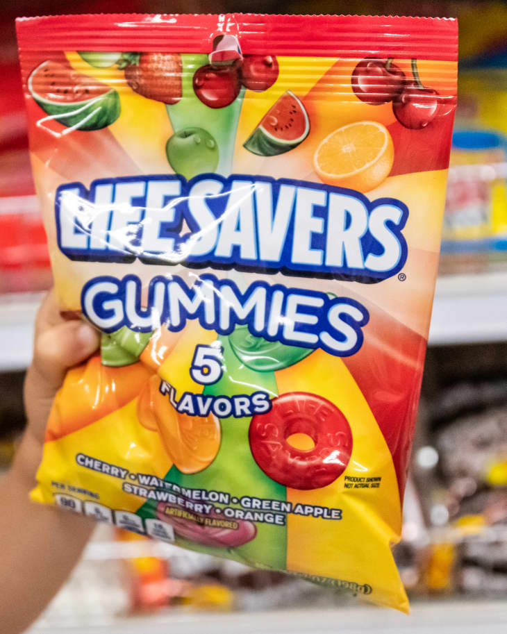 Child's hand holding a bag of Lifesavers brand gunnies candy in a supermarket aisle