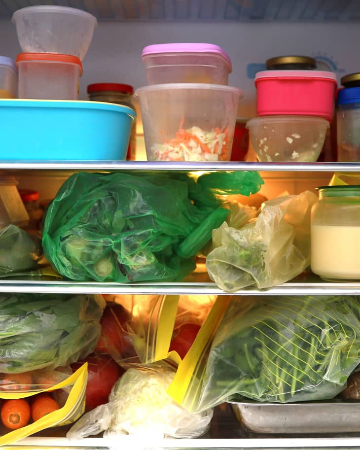 Plastic bags and container with frozen food and vegetables in refrigerator background.