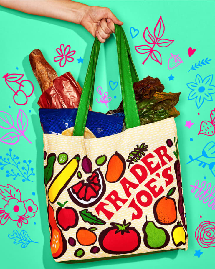 Hand holding Trader Joe's bag with groceries in it on green floral background