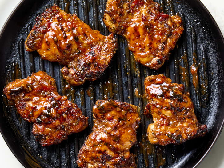 Grilled chicken thighs with a glossy barbecue glaze on a black grill pan.