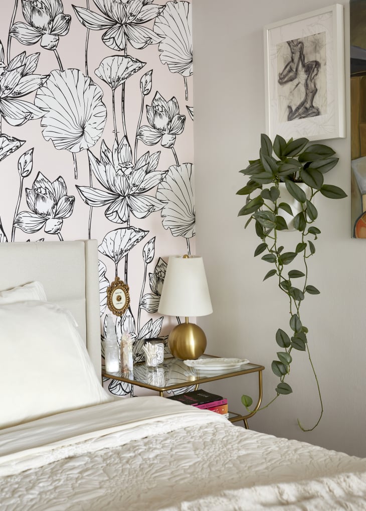 Bedroom with floral wallpaper, gold lamp on glass nightstand, and hanging plant.