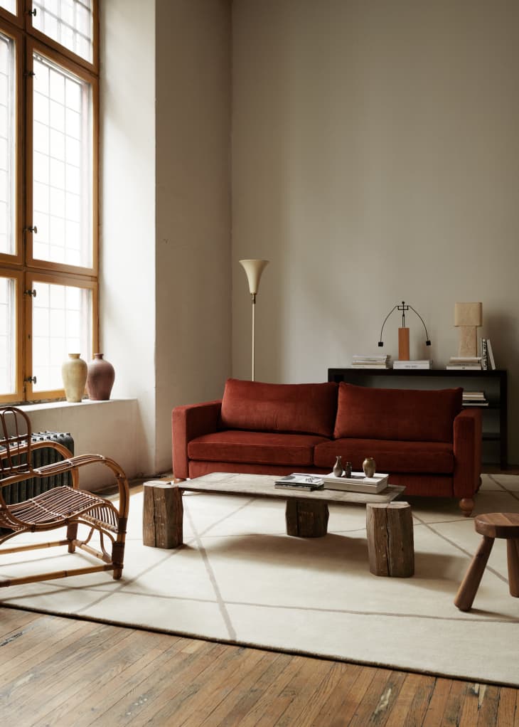 Living room with a red sofa, wooden coffee table, wicker chair, and tall lamp, near large windows and a console table.