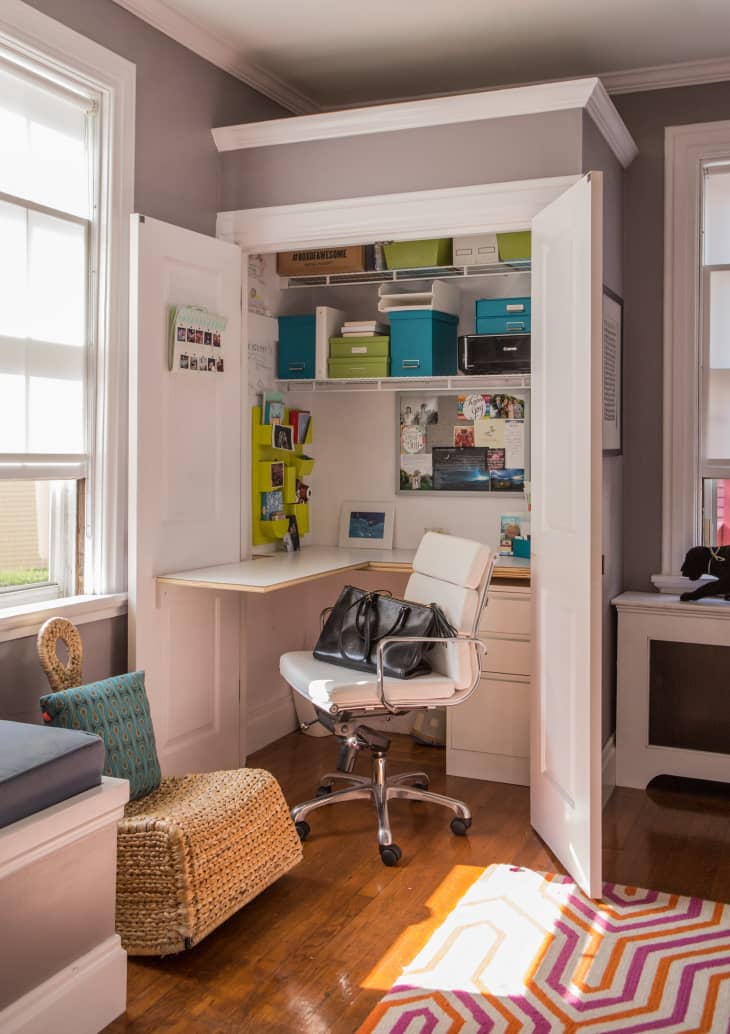 Home office nook with white desk, swivel chair, storage boxes, and decor in a closet space with open doors.