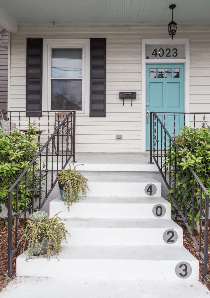Front porch with turquoise door, house number 4023, black shutters, potted plants on steps, and iron railings.