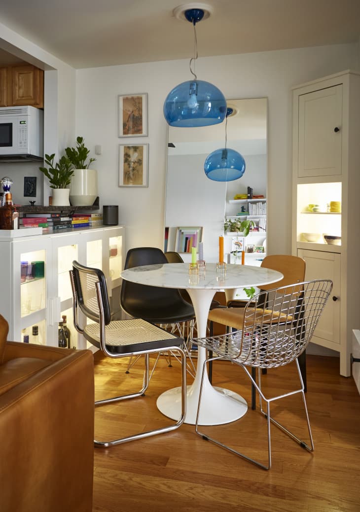 Dining area with a round white table, mixed chairs, blue pendant lights, and a large mirror reflecting bookshelves.