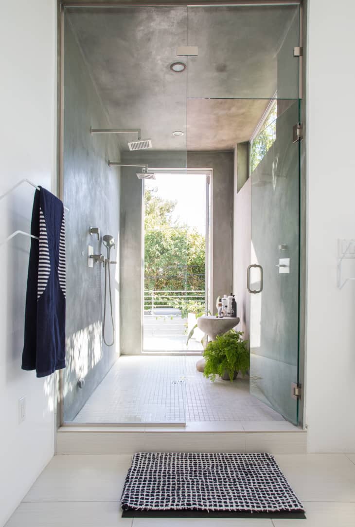 Modern bathroom with glass shower, concrete walls, striped towel, potted fern, and window view of greenery.
