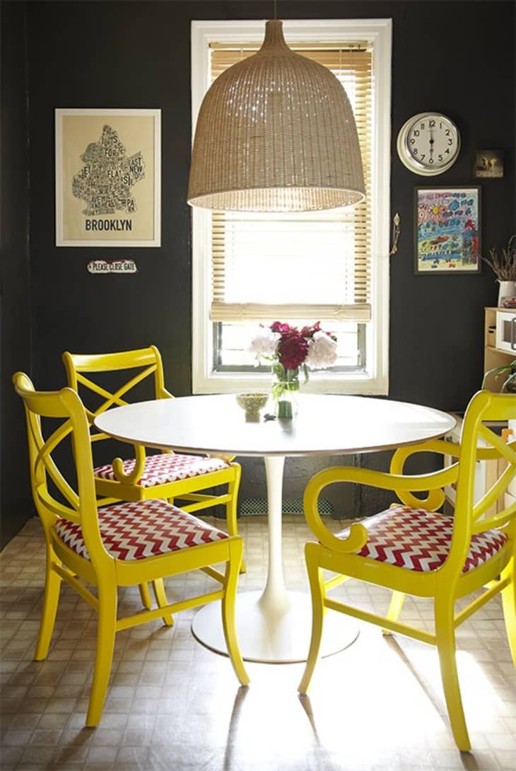 Dining area with a round white table, yellow chairs, red chevron cushions, and a large woven pendant light.