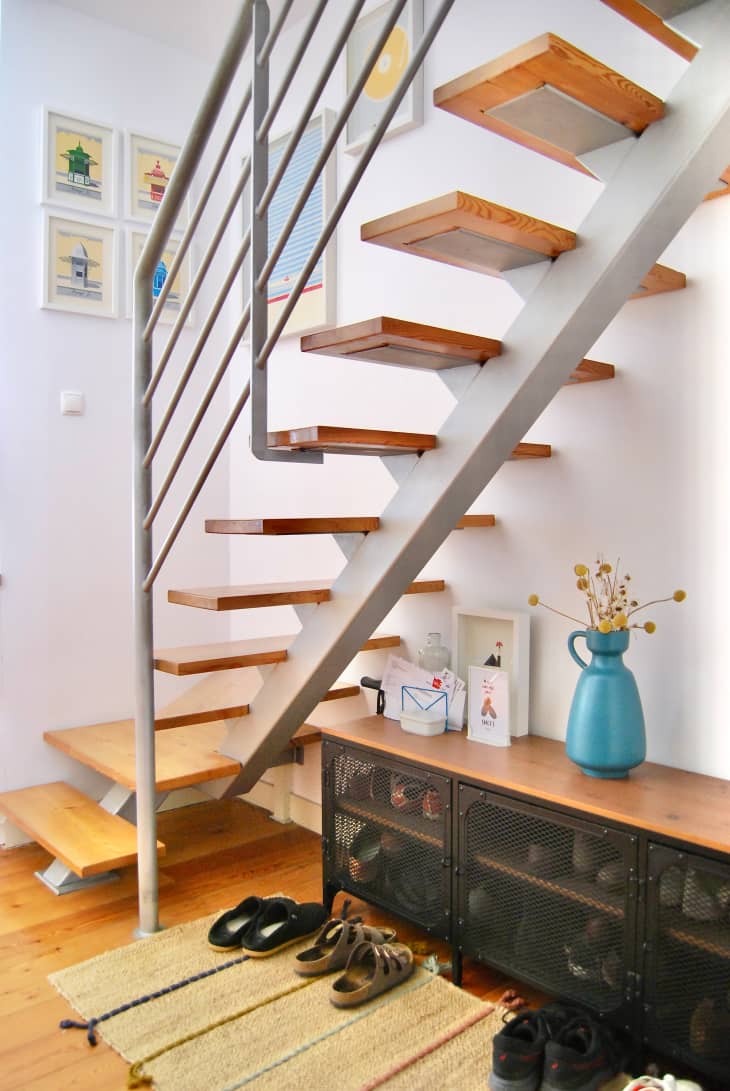 Shoe storage under floating staircase in white room.