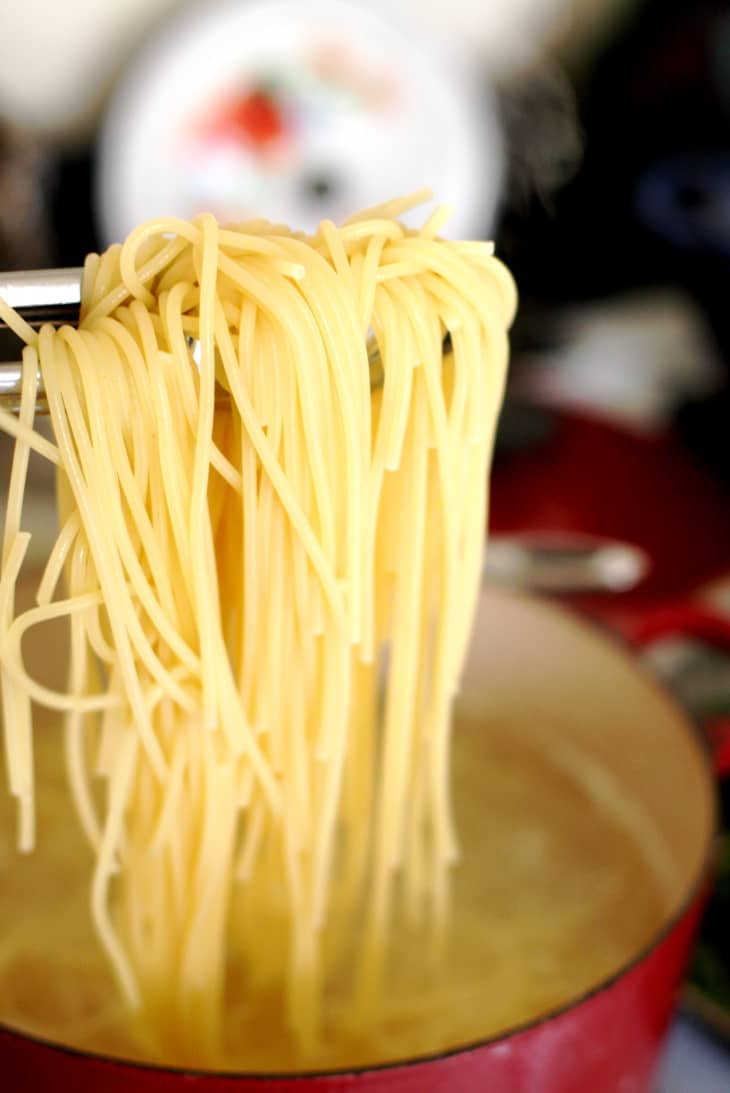 Tongs pulling cooked spaghetti noodles out of a pot of water