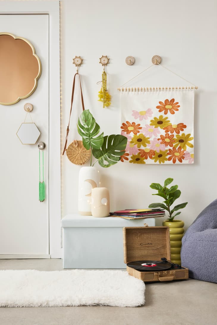Entryway with floral wall art, decorative hooks, a record player, and a potted plant on a light blue bench.