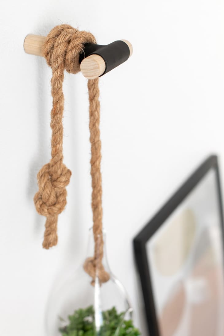 Rope tied on a wooden wall hook with a hanging glass vase containing greenery.